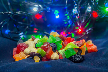Lots of delicious multi-colored candies with nuts on a black background with multi-colored garlands on the background