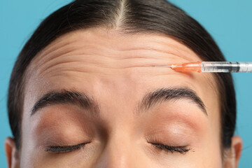 Young woman getting facial injection on light blue background, closeup. Cosmetic surgery