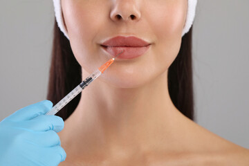 Doctor giving lips injection to young woman on light grey background, closeup. Cosmetic surgery