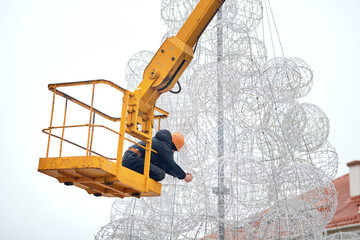 Unknown municipal worker in crane bucket dismantling unusual Christmas tree after winter holidays....