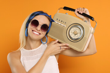 Happy hippie woman with retro radio receiver on orange background