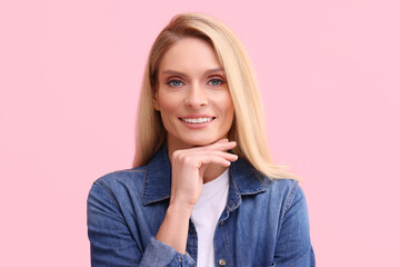 Portrait of smiling middle aged woman with blonde hair on pink background