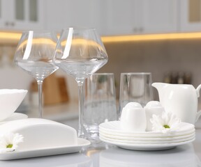 Set of clean dishware, glasses and flowers on table in kitchen
