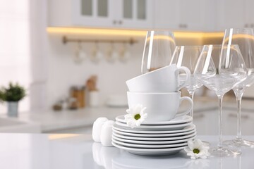 Set of clean dishware, glasses and flowers on table in kitchen, space for text
