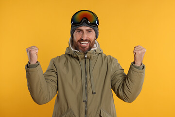 Winter sports. Cheerful man in ski suit and goggles on orange background © New Africa