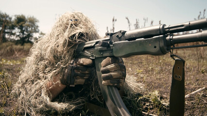 A close-up of a sniper wearing a camouflage suit or grass cloak, waiting and looking through a...