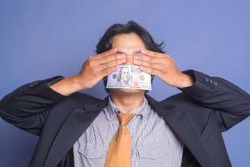 Young man in suits covering his eyes with his hands and his mouth sealed by a hundred dollar bills