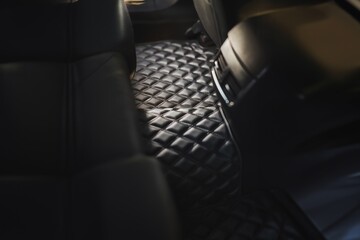 A sophisticated and luxurious leather floor mat in the second row of a modern car. The interior is black and elegant, with a dashboard that has technology and safety features, a seat, and pedals. - obrazy, fototapety, plakaty