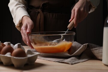 Woman whisking eggs in bowl at table, closeup