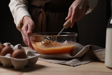 Woman whisking eggs in bowl at table, closeup