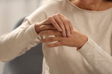 Mature woman suffering from pain in hand on blurred background, closeup. Rheumatism symptom