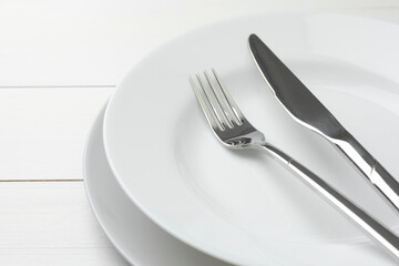 Clean plates, fork and knife on white wooden table, closeup