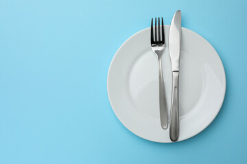 Clean plate, fork and knife on light blue background, top view. Space for text