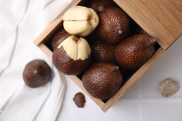 Wooden crate with fresh salak fruits on white tiled table, top view