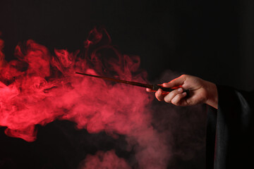 Magician holding wand in smoke on dark background, closeup - obrazy, fototapety, plakaty