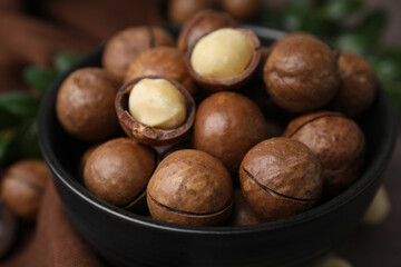 Tasty Macadamia nuts in bowl on brown table, closeup