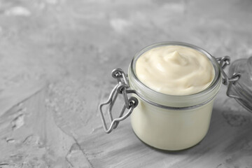 Tasty mayonnaise in jar on gray textured table, closeup. Space for text