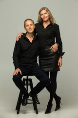 Portrait of a mature couple. Couple, two friends an elderly gray-haired man and a blonde woman in black clothes posing, isolated on a gray background, studio portrait