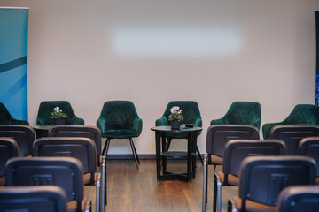  simple seminar setup with a line of luxurious green velvet armchairs behind a small round table, a potted plant on top, and blue graphic roll-up banners to the side.
