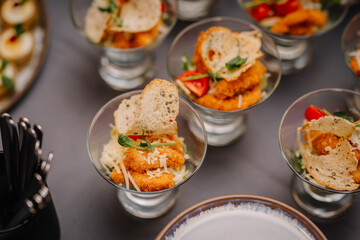 close-up of individual glasses filled with appetizers, garnished with bread crisps and fresh herbs.