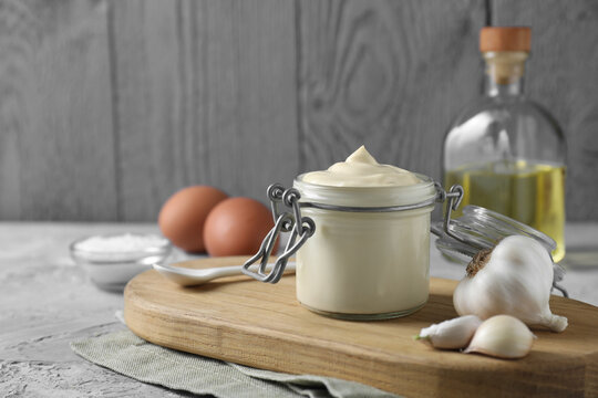 Tasty mayonnaise in jar and garlic on table, closeup. Space for text