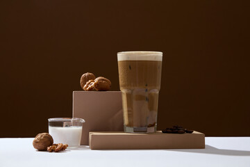 On a dark brown background, a cup of coffee with rich cream is decorated with walnuts, roasted coffee beans and milk. Advertising photo. Coffee has become the spiritual drink of many Vietnamese