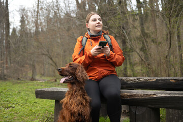 Active happy woman with irish setter dog sitting near on the wood, autumn forest background. Active...