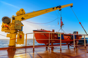 Orange rescue boat on big cargo vessel and crane. Man over board drill. Lifeboat training.