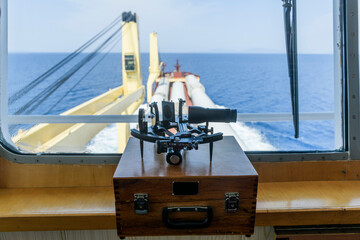 Nautical black sextant placed on wooden box in navigational bridge. Navigational equipment. Celestial navigation.