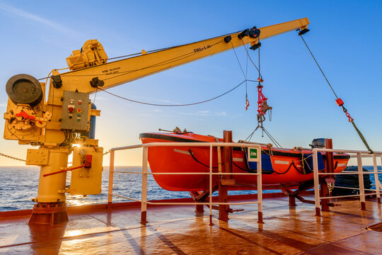 Orange rescue boat on big cargo vessel and crane. Man over board drill. Lifeboat training.
