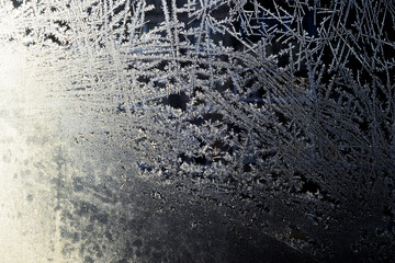 Frosty patterns on the window. Snow crystals. Winter New Year patterns on the window. Nordic realistic snow patterns illuminated by the sun. Golden lighting. Background for a Christmas card.