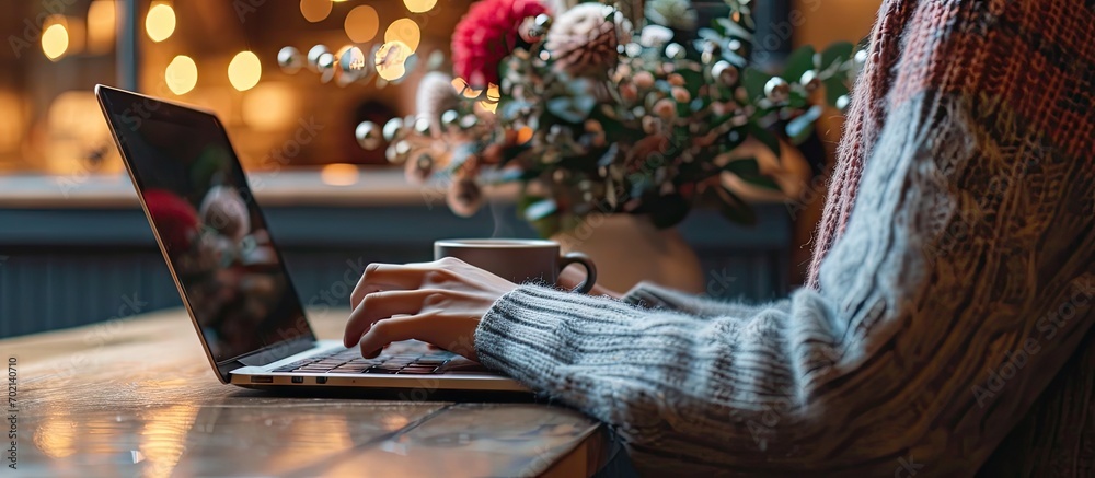 Poster female person sitting at wooden table and holding cup of hot drink while surfing the internet on not