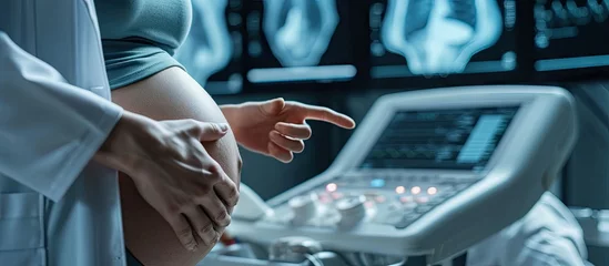 Poster Cropped shot of a pregnant woman during ultrasound scanning at the fertility clinic Female doctor pointing at the screen of ultrasound machine Focus on ultrasound transducer on the pregnant bel © vxnaghiyev