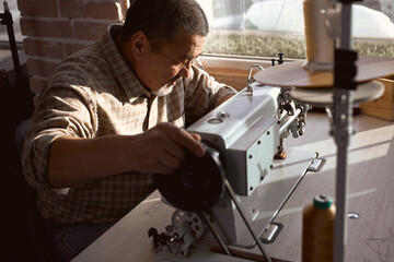 old man preparing leather goods for sale, tailor sews clothing, man creates new garments. close up side view portrait