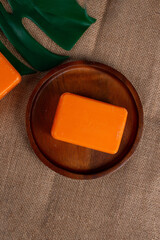 Orange soap on wooden table and and tropical monstera leaves background 