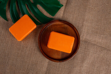 Orange soap on wooden table and and tropical monstera leaves background 