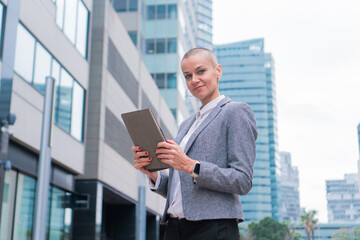 Portrait of businesswoman looking at camera wearing a suit and smiling confident using a tablet outside the corporate building. Manager female with determination and trust standing with a digital pad