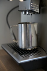 Coffee machine flushes hot water into a silver milk jug
