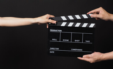 Hands send and hold Black clapper board or movie slate on black background.