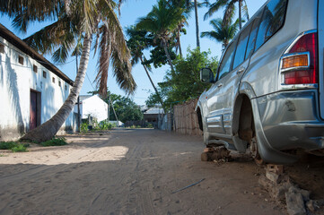 small backroad in Inhambane Mozambique with palm trees and a car without tires