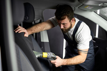 Details of car vacuum cleaning. Professional cropped male worker using wet vacuum cleaner for dirty...