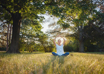Naklejka na ściany i meble Young asian woman doing meditation in morning or evening at park, healthy woman relaxing and practicing yoga at city park. Mindfulness, destress, Healthy habits and balance concept