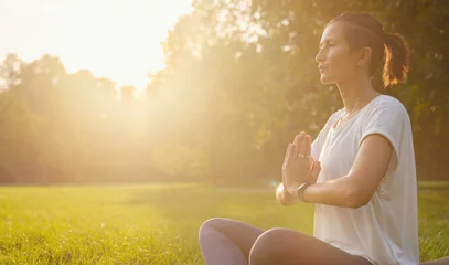 Foto op Plexiglas Young asian woman doing meditation in morning or evening at park, healthy woman relaxing and practicing yoga at city park. Mindfulness, destress, Healthy habits and balance concept © YURII Seleznov