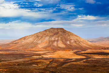 Barren desert landscape with isolated rock formations and volcanic mountains.