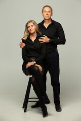 Obraz premium Portrait of a mature couple. Couple, two friends an elderly gray-haired man and a blonde woman in black clothes posing, isolated on a gray background, studio portrait
