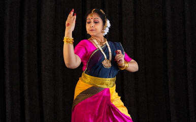 Female Indian classical dancer in traditional costume performing dance mudras on black background