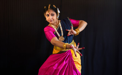 Beautiful Indian classical dancer in traditional costume performing Bharatanatyam dance mudra on black background