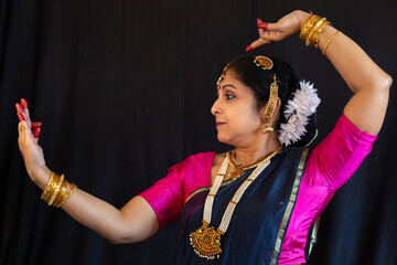 Indian woman classical dancer in traditional costume performing Bharatanatyam dance mudra on black background