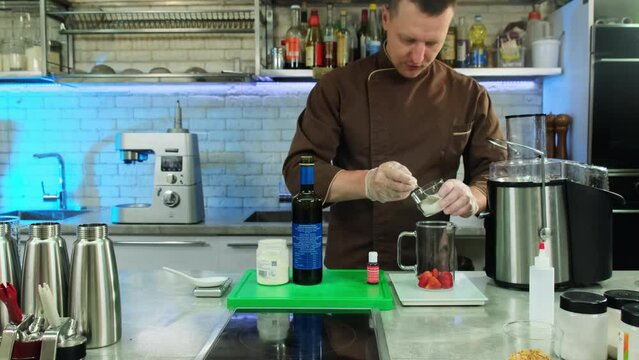 Chef sprinkles powder in jug with fresh strawberries at table. Culinarian prepares ingredients for molecular gastronomy recipe