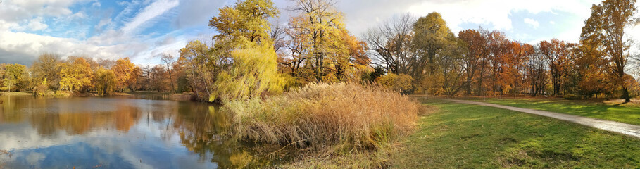 European park and pond in autumn. Atmospheric nature panorama photo.